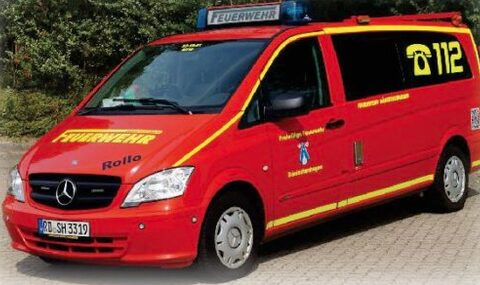 Roter Mercedes-Kleinbus mit gelben Streifen, Blaulichtbalken und der Notrufnummer 112 auf der Seite.