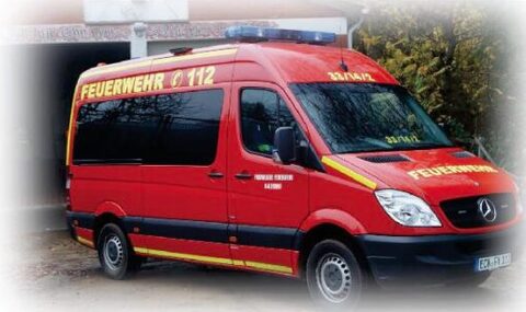 Roter Mercedes-Sprinter mit gelben Streifen, Blaulichtbalken und der Aufschrift „Feuerwehr 112“ vor dem Gerätehaus.