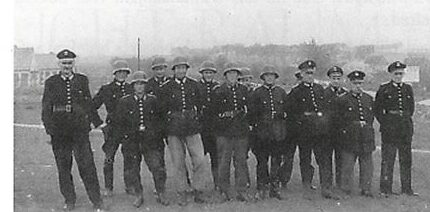 Schwarz-Weiß-Foto 1949: dreizehn Männer in Uniform, einige mit Helm, in einer Reihe auf freiem Feld.