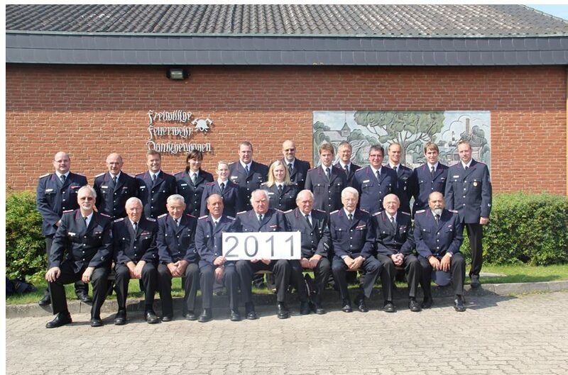Gruppenfoto 2011 vor der Wache: zwei Reihen Feuerwehrleute in Uniform, vorne sitzend hält einer ein Schild mit der Jahreszahl 2011.