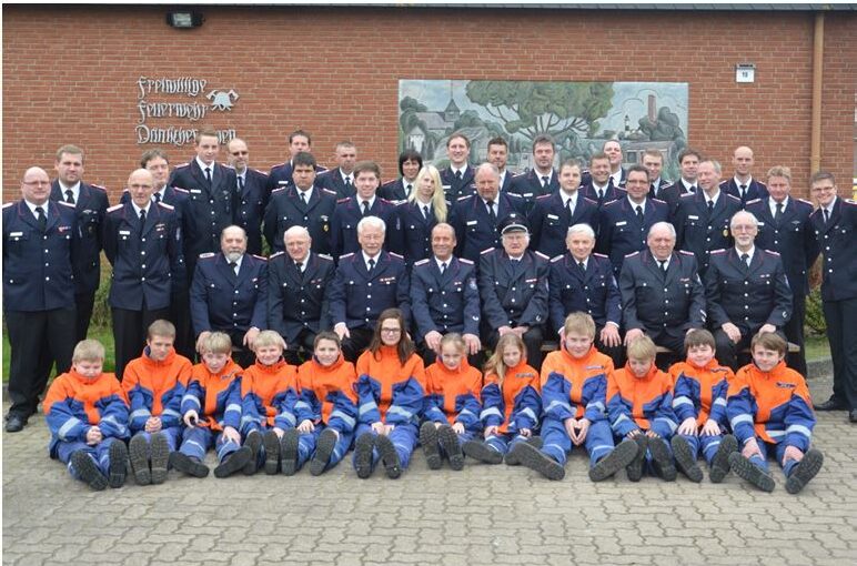 Gruppenfoto 2014 vor der Wache: drei Reihen Feuerwehrleute in dunkelblauer Uniform, davor sitzend die Jugendfeuerwehr in blau-orange.
