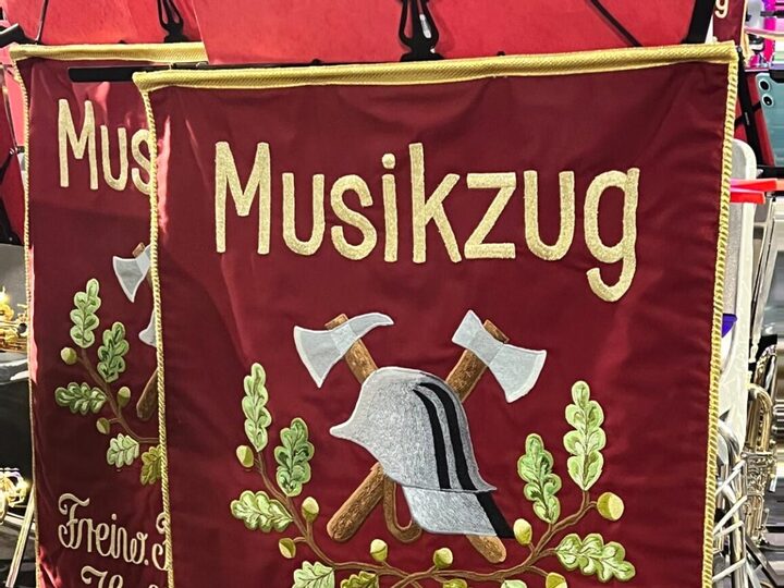 Die weinrote Fahne des Musikzugs mit goldener Stickerei: das Wort Musikzug, ein Feuerwehrhelm mit zwei gekreuzten Beilen und Eichenlaub.