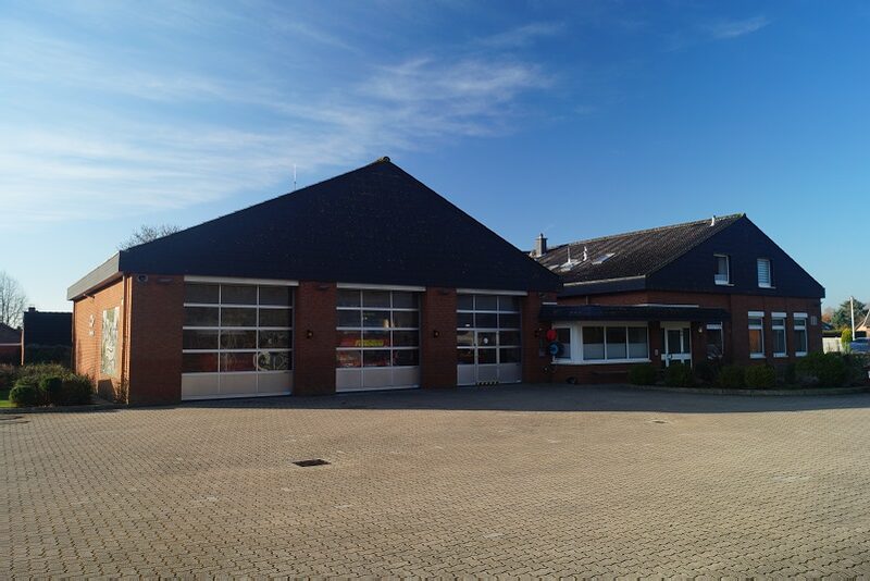 Das Feuerwehrgerätehaus Dänischenhagen: ein Klinkerbau mit spitzem Dach und vier großen Fahrzeugtoren, davor ein gepflasterter Hof.