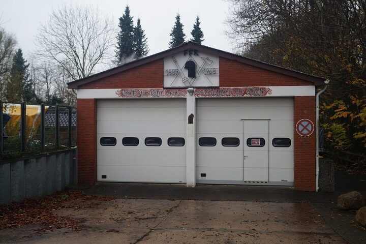 Das Feuerwehrgerätehaus Kaltenhof: ein Backsteinbau mit zwei weißen Rolltoren. Im Giebel die Buchstaben FFK, ein Wappen mit den Jahreszahlen 1889 und 1968 und darunter ein Schriftzug.